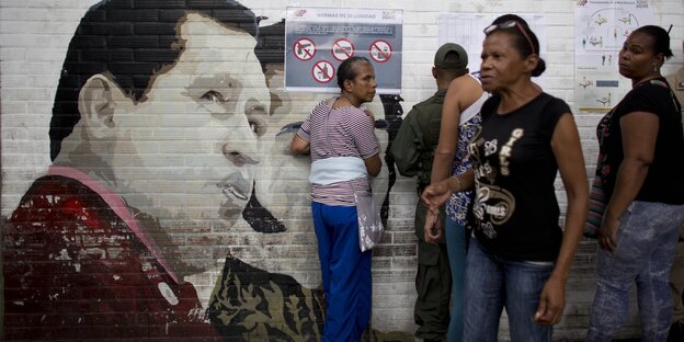 Ein Graffiti von Maduro, daneben stehen mehrere Menschen Ein Graffiti von Maduro, daneben stehen mehrere Menschen