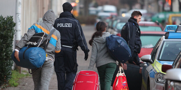 Polizisten geleiten Leute zu einem Fahrzeug Polizisten geleiten Leute zu einem Fahrzeug