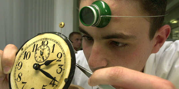 Ein junger Mann mit Stirnlampe repariert eine Uhr Ein junger Mann mit Stirnlampe repariert eine Uhr