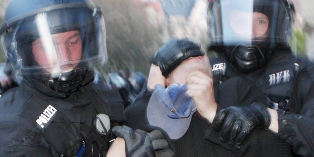 Zwei behelmte Polizisten führen rabiat eine Person ab Zwei behelmte Polizisten führen rabiat eine Person ab