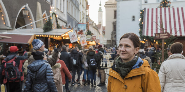 Eine Frau, Eva Wittig, im Hintergrund Besucher eines Weihnachtsmarktes Eine Frau, Eva Wittig, im Hintergrund Besucher eines Weihnachtsmarktes