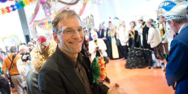 Werner Wölfle grinst in die Kamera, im Hintergrund stehen Narren Werner Wölfle grinst in die Kamera, im Hintergrund stehen Narren