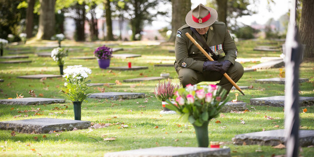 Ein Soldat in Uniform hockt vor einem Grab auf einem Friedhof Ein Soldat in Uniform hockt vor einem Grab auf einem Friedhof