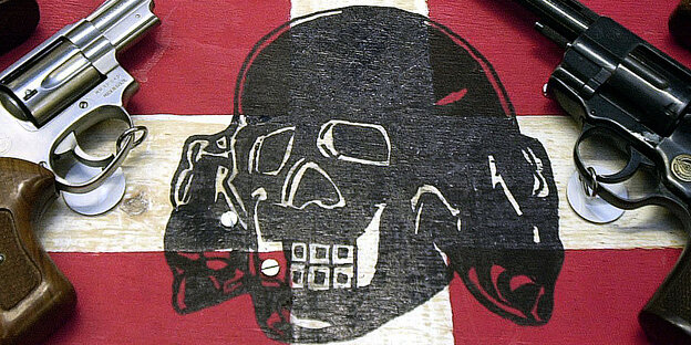 EIne Flagge mit Totenkopf liegt zwischen zwei Schusswaffen