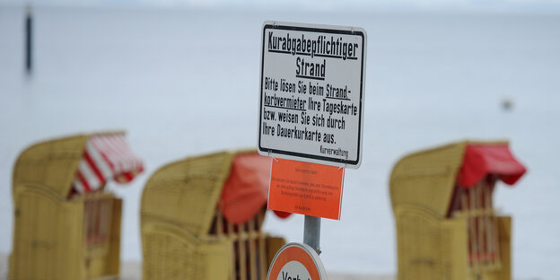 Ein Schild mit dem Hinweis auf eine kostenpflichtige Strandbenutzung steht vor drei Strandkörben. Ein Schild mit dem Hinweis auf eine kostenpflichtige Strandbenutzung steht vor drei Strandkörben.