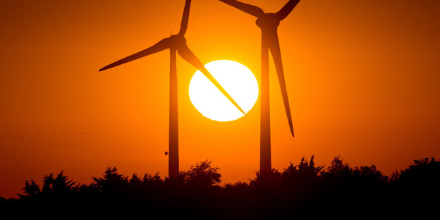 Die Sonne versinkt hinter zwei Windrädern Die Sonne versinkt hinter zwei Windrädern