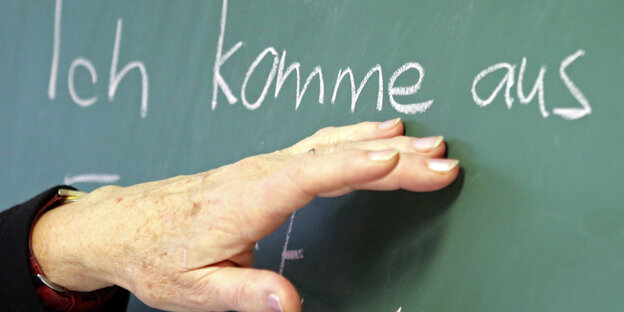 Eine Hand zeigt auf einer Schultafel den Satzteil „Ich komme aus" Eine Hand zeigt auf einer Schultafel den Satzteil „Ich komme aus"