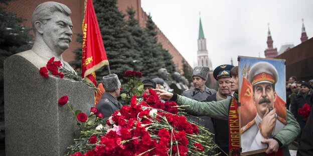 Vor einer Stalinstatue liegen rote Rosen, eine Frau hält ein Porträt von ihm im Arm Vor einer Stalinstatue liegen rote Rosen, eine Frau hält ein Porträt von ihm im Arm