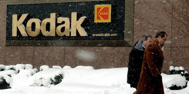Zwei Männer im Schnee, hinten ein Kodak-Logo an einer Hauswand Zwei Männer im Schnee, hinten ein Kodak-Logo an einer Hauswand