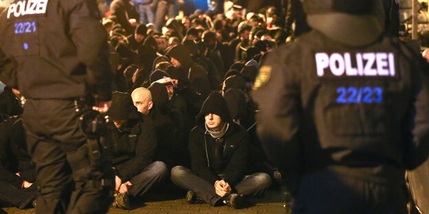 Zahlreiche Männer sitzen gefesselt vor Polizisten auf der Straße Zahlreiche Männer sitzen gefesselt vor Polizisten auf der Straße