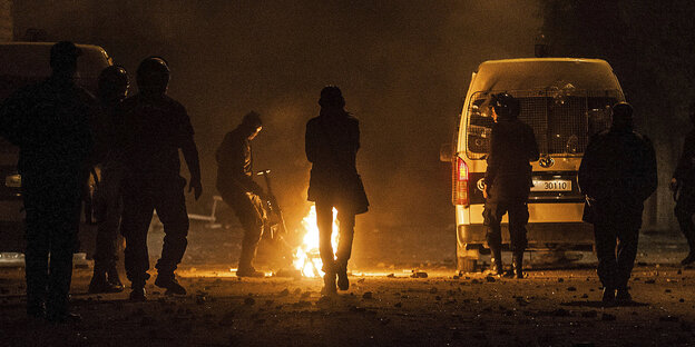 Mehrere uniformierte Polizisten um ein Feuer neben einem Auto in der Nacht Mehrere uniformierte Polizisten um ein Feuer neben einem Auto in der Nacht