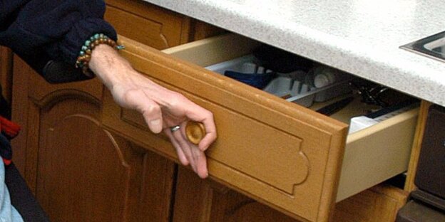 Eine Hand greift an eine Schublade und zieht sie auf. Eine Hand greift an eine Schublade und zieht sie auf.