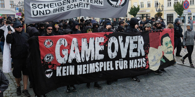 Eine Menschenmenge mit einem Transparent mit der Aufschrift "Game Over" auf einem Platz in einer Kleinstadt Eine Menschenmenge mit einem Transparent mit der Aufschrift "Game Over" auf einem Platz in einer Kleinstadt