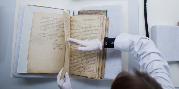 Eine Person mit Handschuhen hält ein altes Buch offen Eine Person mit Handschuhen hält ein altes Buch offen