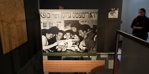 Eine Gruppe Menschen, die unter einem hebräischen Schriftzug in einer Zeitung lesen.