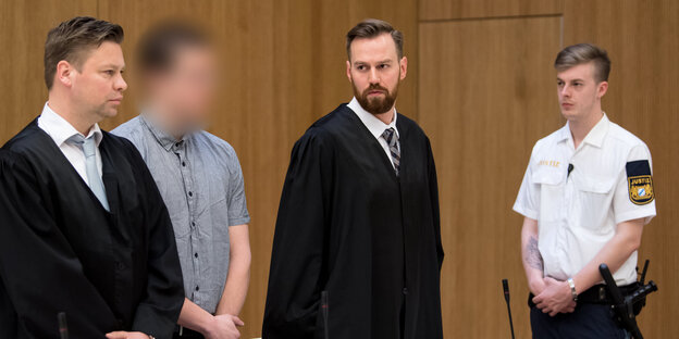 Vier Männer stehen nebeneinander: Zwei in Anwaltsroben, einer in Zivil, einer in Uniform Vier Männer stehen nebeneinander: Zwei in Anwaltsroben, einer in Zivil, einer in Uniform