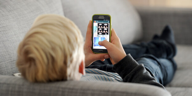 Ein Kind liegt auf dem Sofa und tippt auf seinem Smartphone Ein Kind liegt auf dem Sofa und tippt auf seinem Smartphone