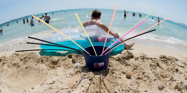 Ein Eimer mit vielen langen Strohhalmen am Sandstrand