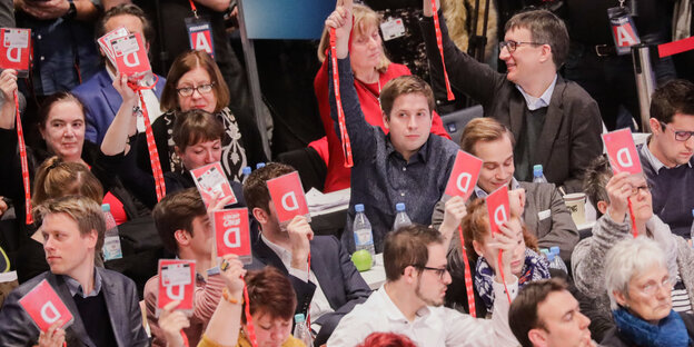 Viele Menschen sitzen in Reihen hintereinaner und halten je eine Karte hoch