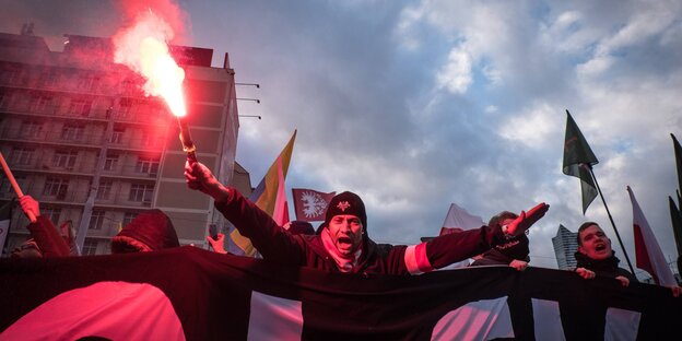 Ein Mann hinter einem Banner hält einen Bengalo in die Luft. Ein Mann hinter einem Banner hält einen Bengalo in die Luft.
