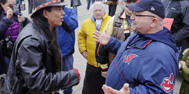 Zwei Männer stehen sich gegenüber und diskutieren, der rechte trägt auf seiner Jacke das alte Logo der Cleveland Indians Zwei Männer stehen sich gegenüber und diskutieren, der rechte trägt auf seiner Jacke das alte Logo der Cleveland Indians