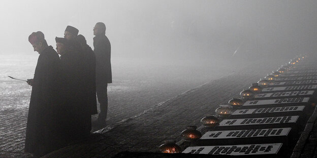 Menschen stehen in Nebel an der Gedenkstätte des ehemaligen Konzentrationslagers Auschwitz Menschen stehen in Nebel an der Gedenkstätte des ehemaligen Konzentrationslagers Auschwitz