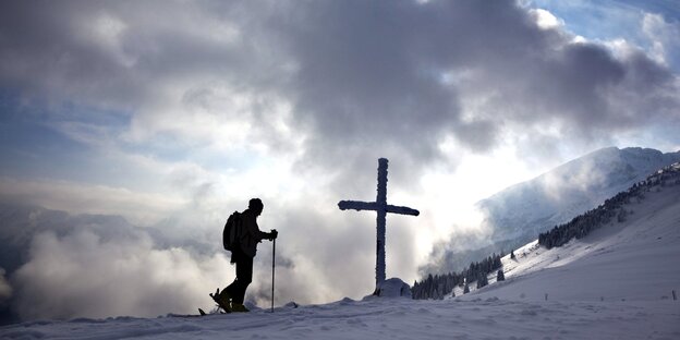 Silhouette einer Skiläuferin vor einem Kreuz im Schnee Silhouette einer Skiläuferin vor einem Kreuz im Schnee