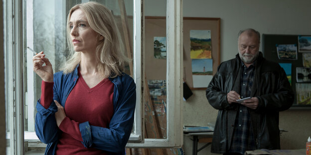 Kommissar Jakob Franck steht im Hintergrund und befragt die Schwester der Toten. Diese steht am Fenster und raucht. Kommissar Jakob Franck steht im Hintergrund und befragt die Schwester der Toten. Diese steht am Fenster und raucht.