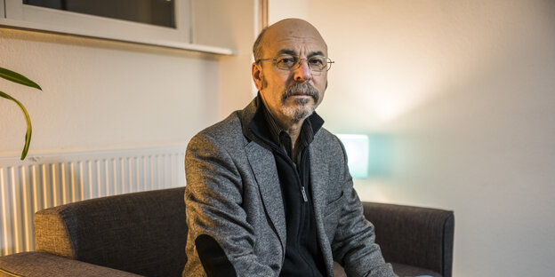 Ein Mann mit Brille, grauem Bart und Glatze sitzt auf einem dunklen Sessel. Ein Mann mit Brille, grauem Bart und Glatze sitzt auf einem dunklen Sessel.