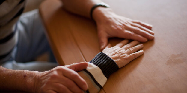 Hände führen die Hand einer älteren Person über eine Tischplatte Hände führen die Hand einer älteren Person über eine Tischplatte