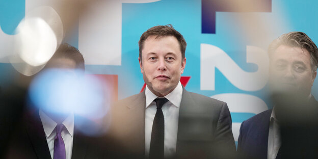 Elon Musk bei einer Messe. Zwei Männer neben ihm unscharf Elon Musk bei einer Messe. Zwei Männer neben ihm unscharf