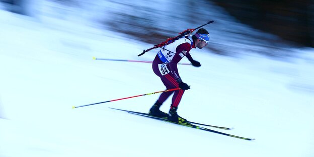 Biathlet, der auf Skiern schnell einen Berg herunterfährt Biathlet, der auf Skiern schnell einen Berg herunterfährt