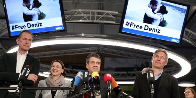 Auf zwei Bildschirmen flimmert das Foto von Deniz Yücel und seiner Frau Dilek, darunter mehrere Personen hinter Mikros Auf zwei Bildschirmen flimmert das Foto von Deniz Yücel und seiner Frau Dilek, darunter mehrere Personen hinter Mikros
