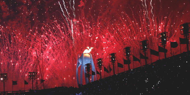ein rotes Feuerwerk über einem Stadion, in der Mitte brennt ein monumentales olympisches Feuer ein rotes Feuerwerk über einem Stadion, in der Mitte brennt ein monumentales olympisches Feuer