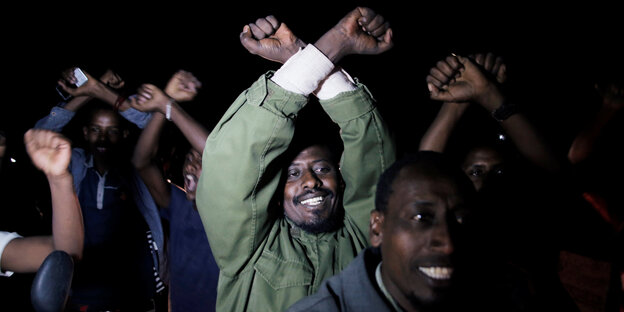 Mehrere afrikanische Männer halten bei Nacht freudestrahlend ihre Arme über dem Kopf gekreuzt. Mehrere afrikanische Männer halten bei Nacht freudestrahlend ihre Arme über dem Kopf gekreuzt.