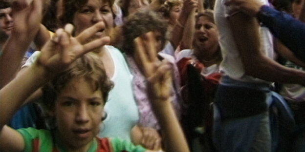 Ein Junge steht in einer Menschenmenge und zeigt das Victory-Zeichen