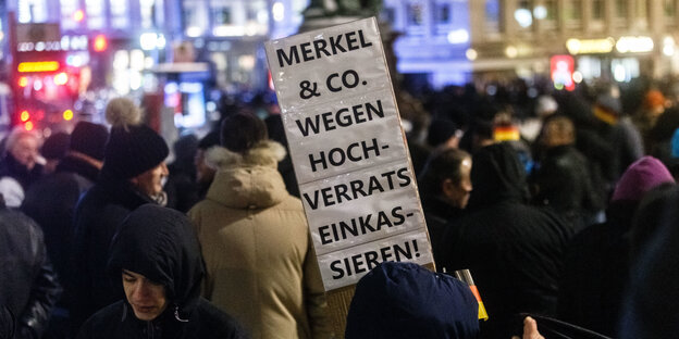 Menschen in Wintermänteln stehen in der Hamburger Innenstadt. Einer hält ein Schild hoch, auf dem steht: "Merkel und Co. wegen Hochverrats einkassieren". Menschen in Wintermänteln stehen in der Hamburger Innenstadt. Einer hält ein Schild hoch, auf dem steht: "Merkel und Co. wegen Hochverrats einkassieren".