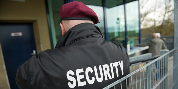 Ein kräftiger Mann lehnt an einem Geländer. Auf seiner Jacke steht "Security". Ein kräftiger Mann lehnt an einem Geländer. Auf seiner Jacke steht "Security".