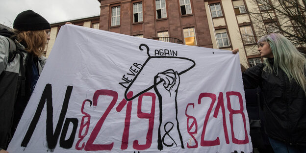 Frauen halten ein Transparent in die Höhe, auf dem „No 219 & 218“ und ein Kleiderbügel zu sehen sind Frauen halten ein Transparent in die Höhe, auf dem „No 219 & 218“ und ein Kleiderbügel zu sehen sind