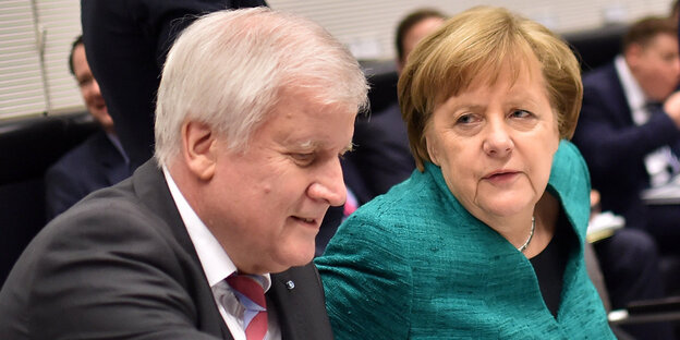 Angela Merkel in meergrünem Blazer und mit genervtem Gesicht neben einem geschäftig guckenden Horst Seehofer