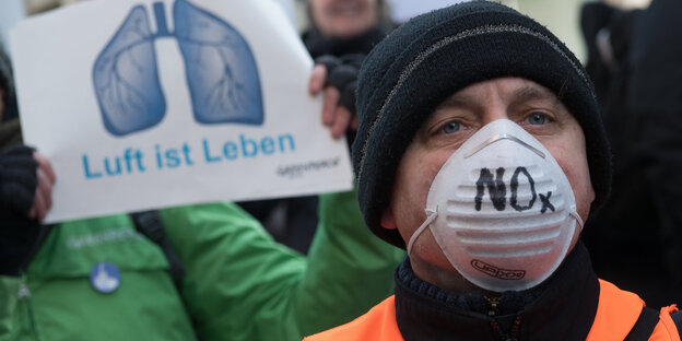 Mann mit schwarzer Mütze und weißer Atemmaske. Auf der Maske steht NOx Mann mit schwarzer Mütze und weißer Atemmaske. Auf der Maske steht NOx