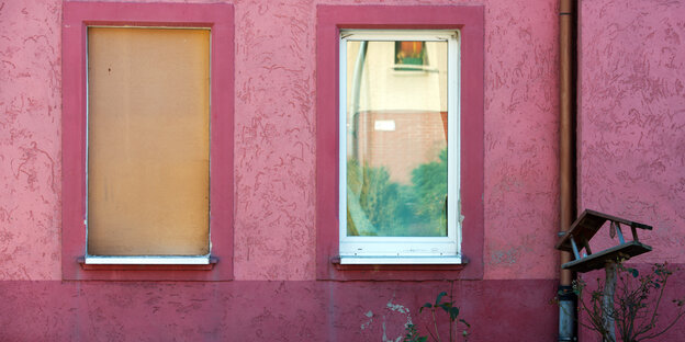 Eine pinke Hauswand, zwei Fenster sind mit Holz versperrt Eine pinke Hauswand, zwei Fenster sind mit Holz versperrt