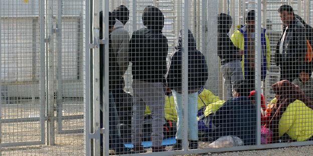 Menschen hinter einem Grenzzaun Menschen hinter einem Grenzzaun