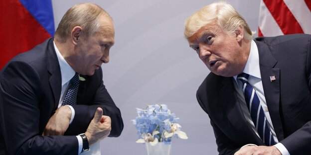 Putin und Trump sitzen an einem Tisch und lehnen sich aufeinander zu Putin und Trump sitzen an einem Tisch und lehnen sich aufeinander zu
