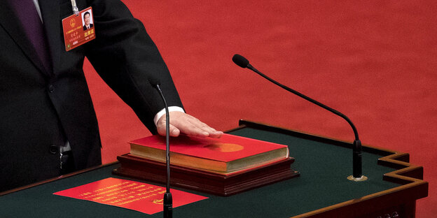 Ein rotes Buch auf einem Pult mit Mikrofon. Eine Hand liegt darauf. Man sieht nur den Arm des Mannes Ein rotes Buch auf einem Pult mit Mikrofon. Eine Hand liegt darauf. Man sieht nur den Arm des Mannes