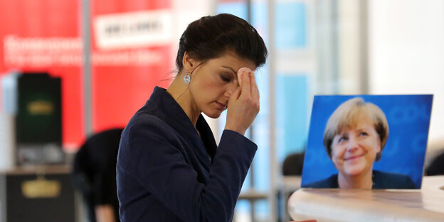 eine Frau tupft sich die Stirn, neben ihr ein Bild der lächelnden Angela Merkel