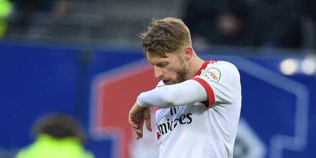 Ein junger Mann mit weiß-rotem Fußballtrikot und blonden Haaren wischt sich mit dem Arm über das Gesicht. Ein junger Mann mit weiß-rotem Fußballtrikot und blonden Haaren wischt sich mit dem Arm über das Gesicht.