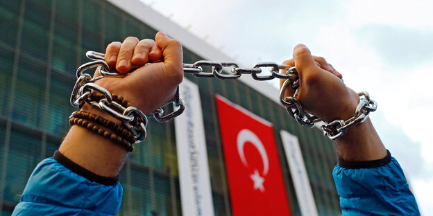 Hände, die eine Kette in die Höhe halten vor einem Gebäude, an dem die türkische Flagge hängt Hände, die eine Kette in die Höhe halten vor einem Gebäude, an dem die türkische Flagge hängt