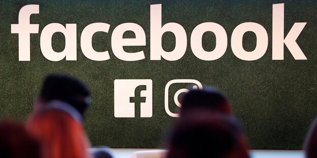 Ein Facebooklogo an einer Wand, darunter stehen Menschen Ein Facebooklogo an einer Wand, darunter stehen Menschen