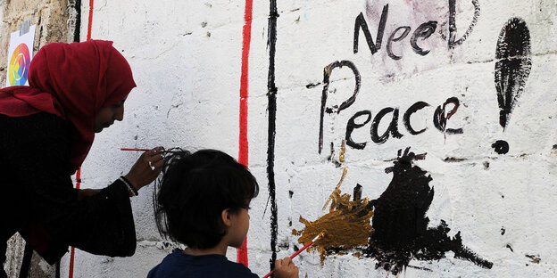 Eine Frau und ein Kind malen während einer Kunstaktion Gaffiti an eine Wand an der "Need Peace!" Eine Frau und ein Kind malen während einer Kunstaktion Gaffiti an eine Wand an der "Need Peace!"